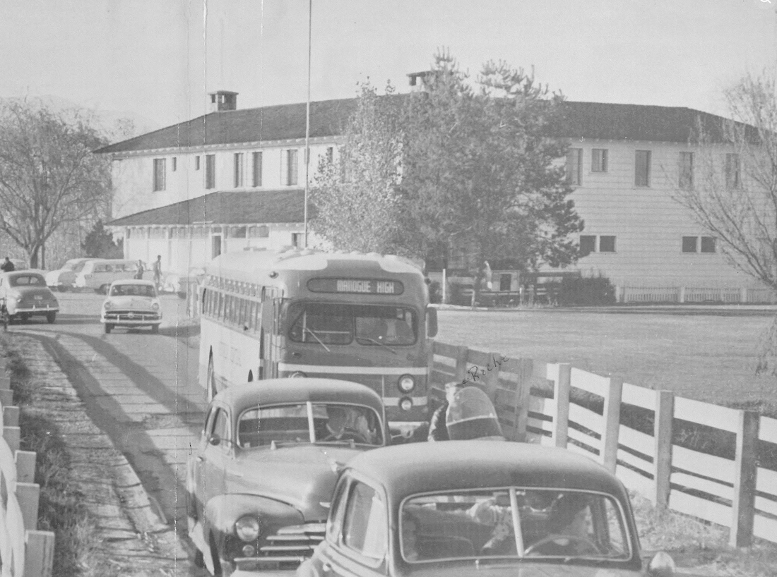 A bus with MANOGUE HIGH on its destination board waits outside the former Flick Ranch mansion on Glendale Road, Reno, about 1950, when the house was the first Bishop Manogue High School. Cars of the period are parked along a white board fence.