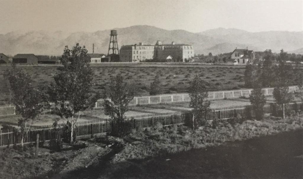 The Nevada State Insane Asylum near Reno, photographed about 1900 from the south-east across its own farm fields, with the main brick building and its water tower against the Virginia Range.