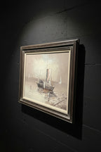 Framed painting of a ship on a dock with a decorative metal stand in the background.