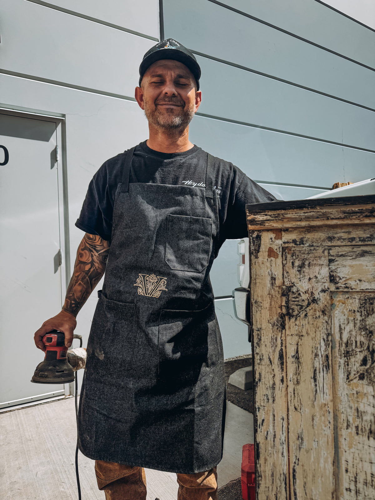 Walter Hinchman in the workshop beside a nineteenth-century painted cabinet, orbital sander in hand, Reno Nevada.
