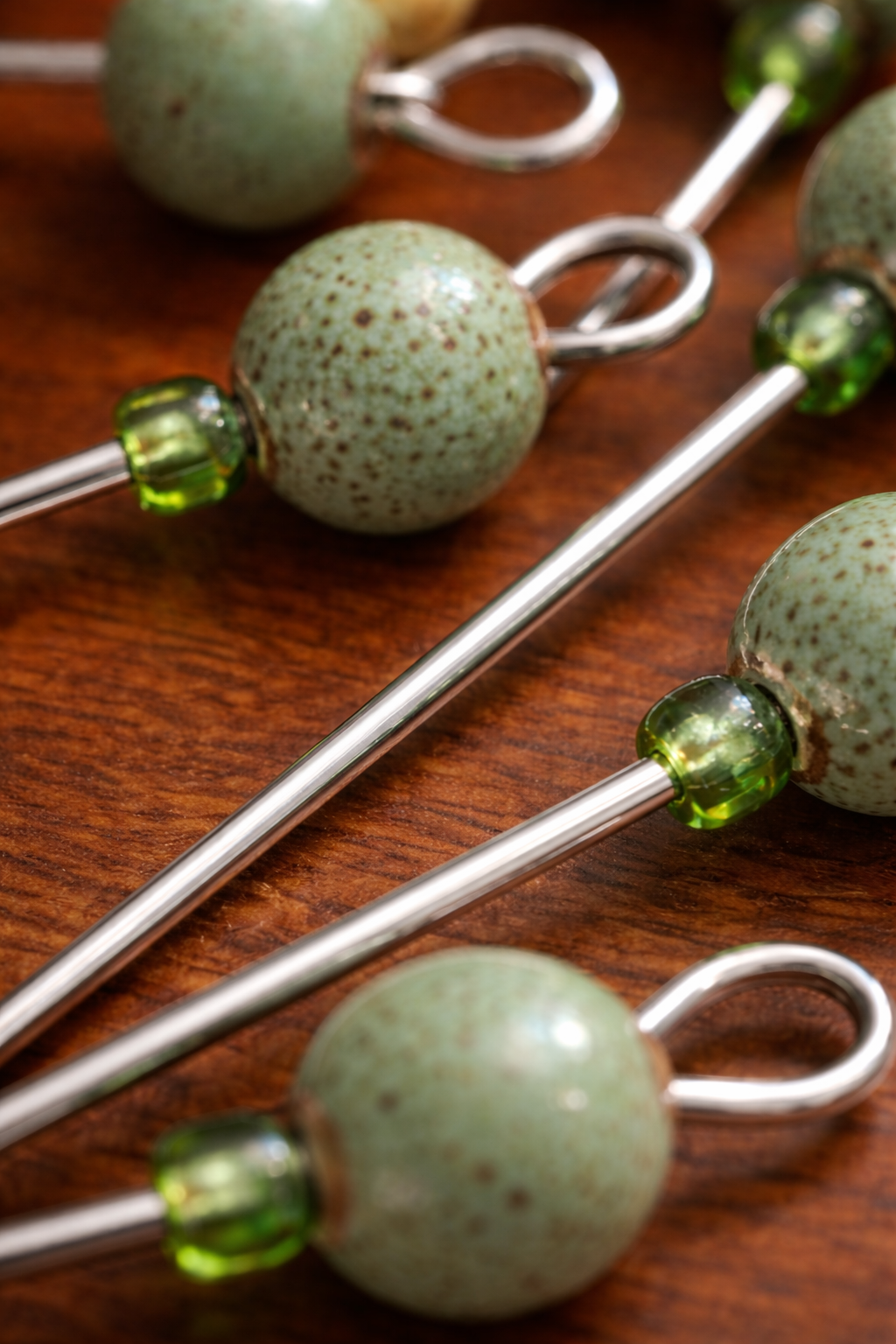 Silver skewers with green and brown speckled beads on a wooden surface